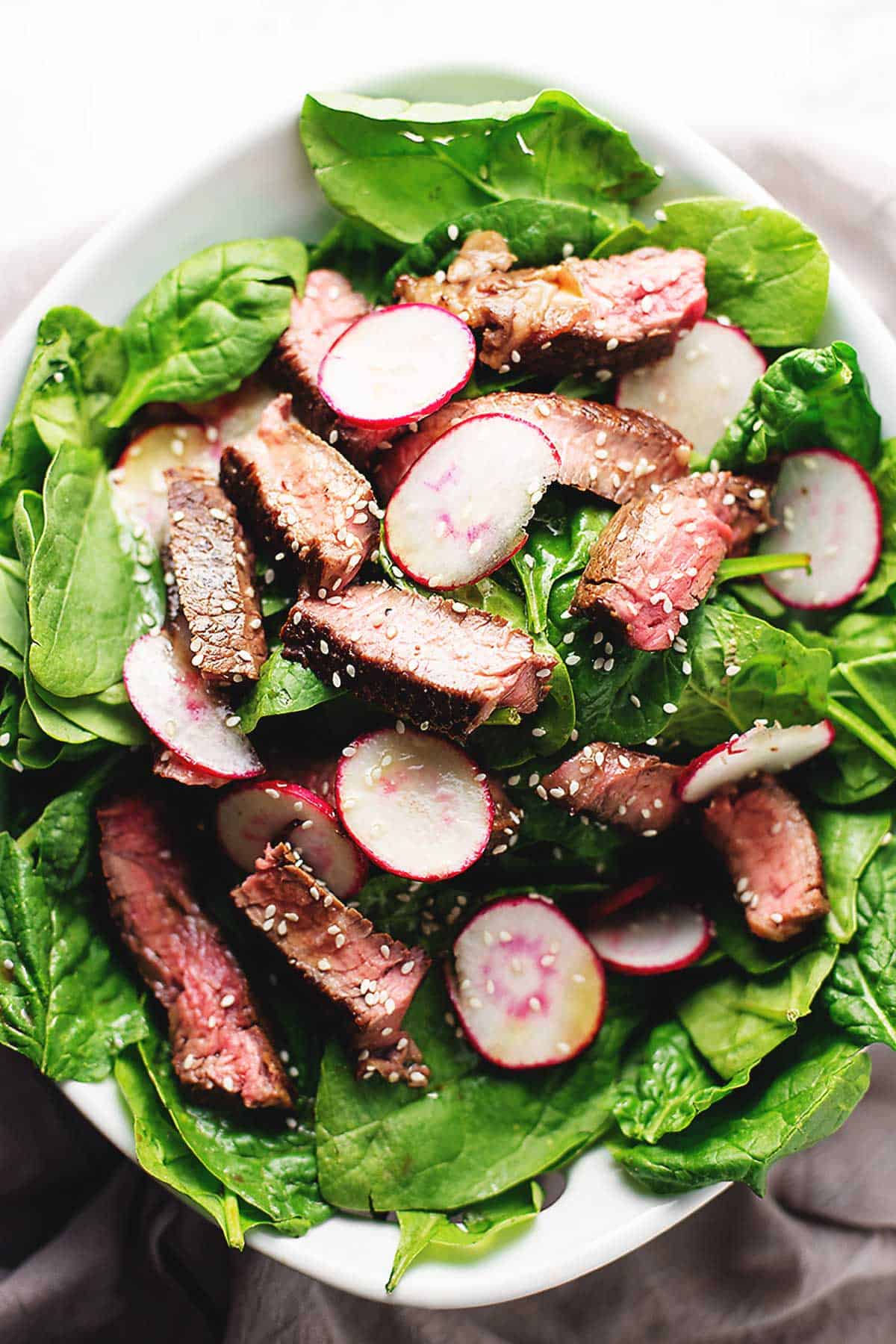 steak salad with radishes and spinach in a serving bowl