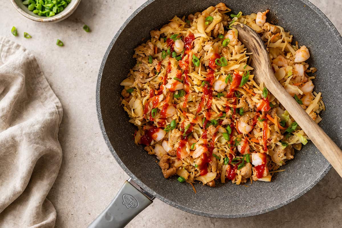 finished egg roll in a bowl topped with scallions and sriracha