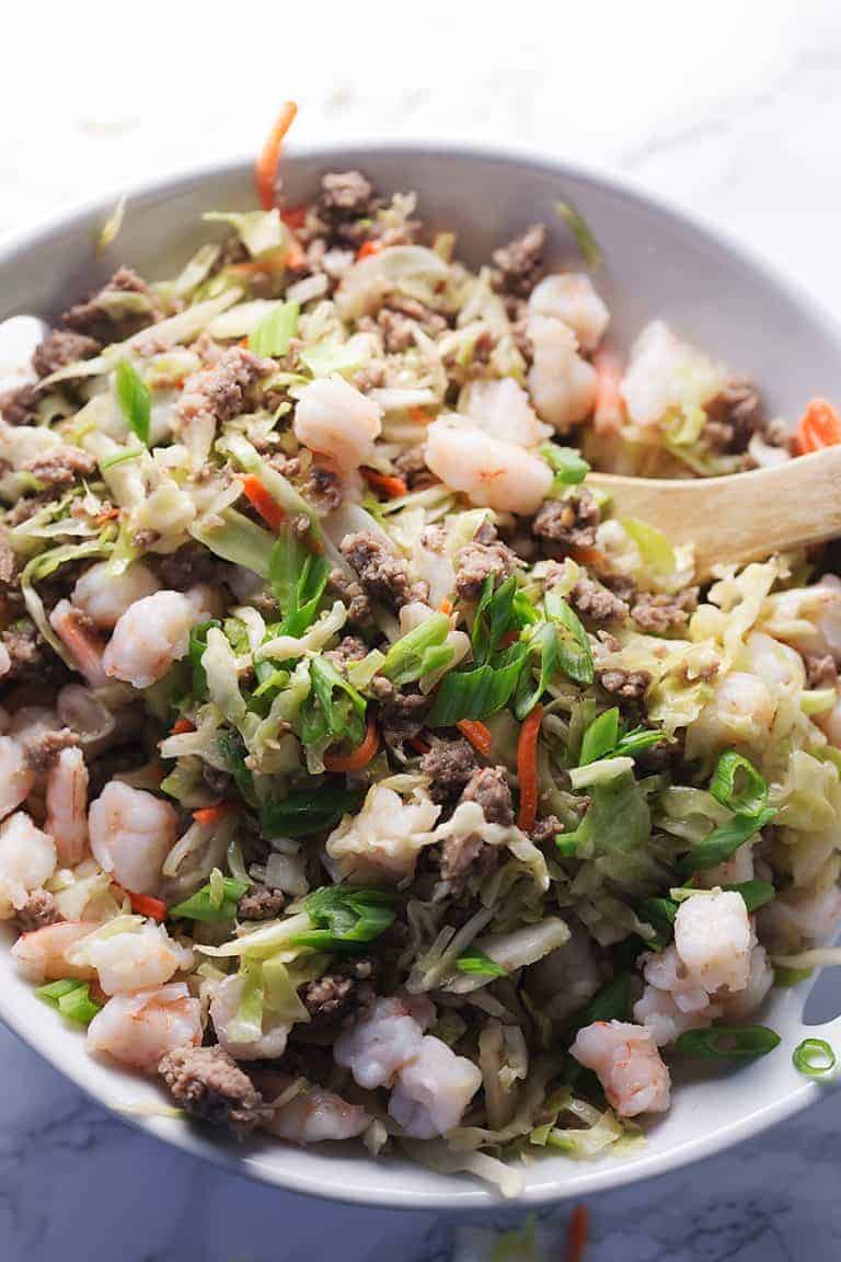 the insides of an egg roll in a white bowl with a wooden spoon