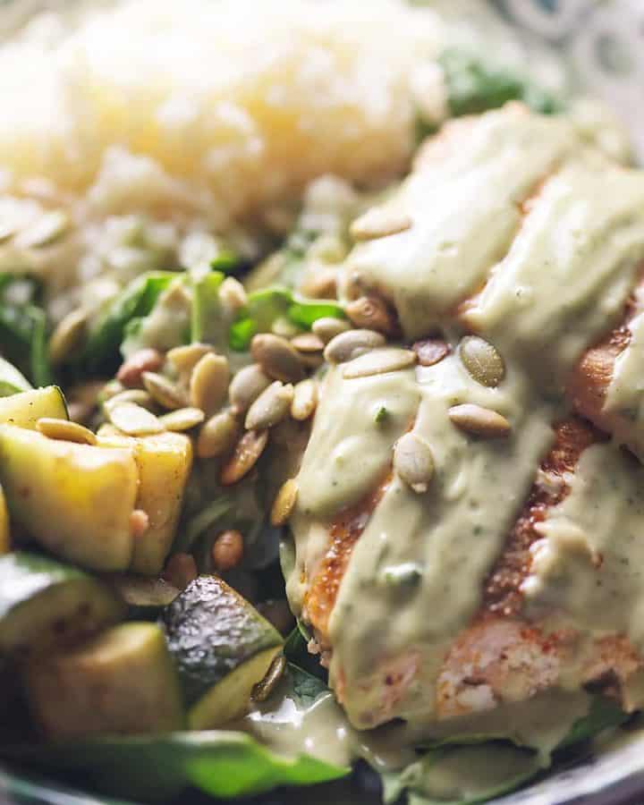 salmon bowl with spinach, roasted zucchini, steamed cauliflower rice, pumpkin seeds and avocado cilantro lime dressing
