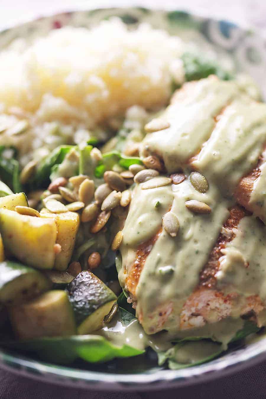 salmon bowl with spinach, roasted zucchini, steamed cauliflower rice, pumpkin seeds and avocado cilantro lime dressing