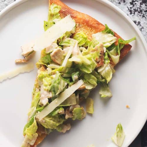 a sliced of chicken caesar salad pizza on a white plate.