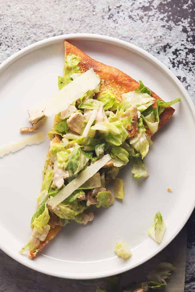 a sliced of chicken caesar salad pizza on a white plate.