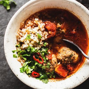 albondigas soup with cilantro and cauliflower rice in a white bowl
