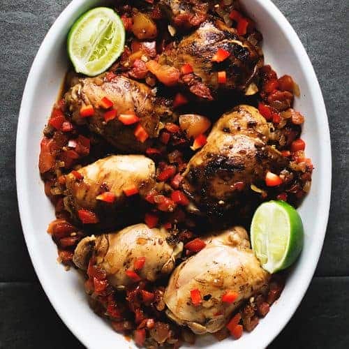 brown stew chicken in a white casserole dish on a dark grey background