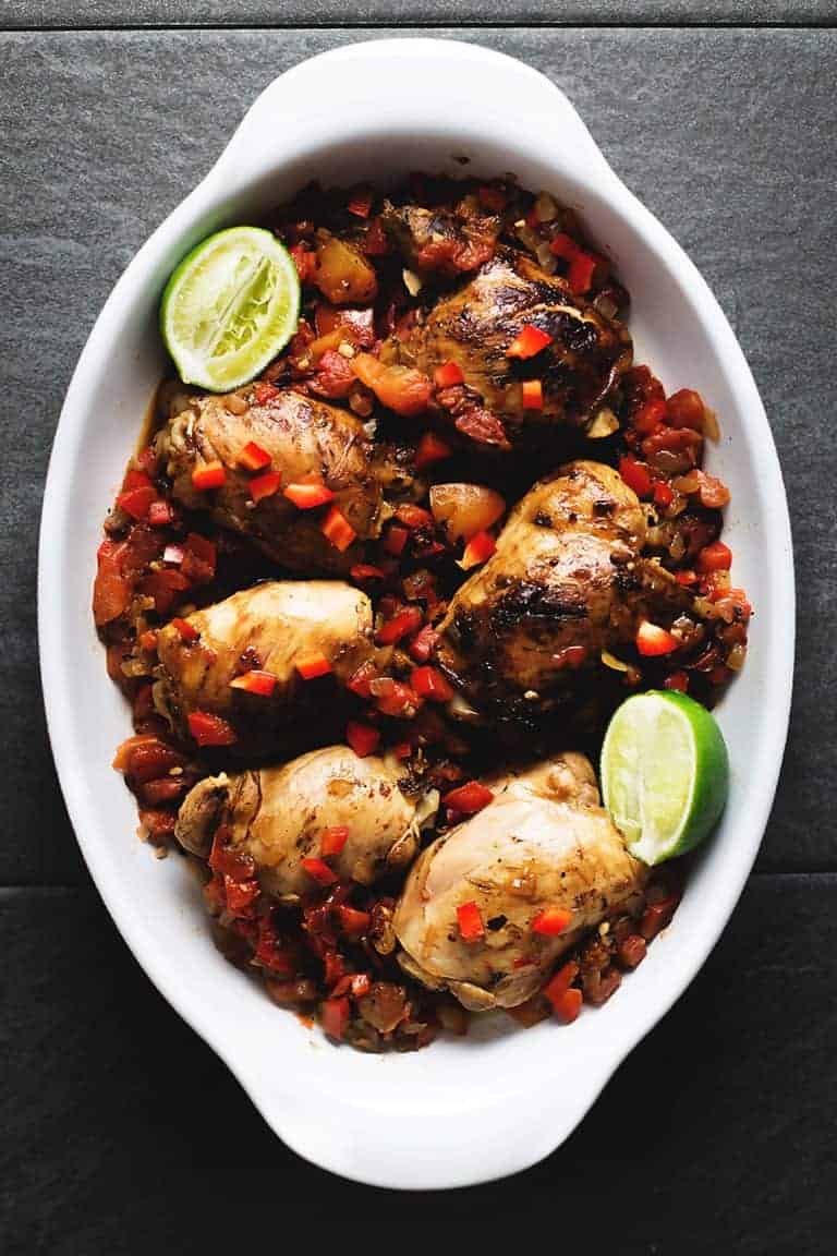 brown stew chicken in a white casserole dish on a dark grey background