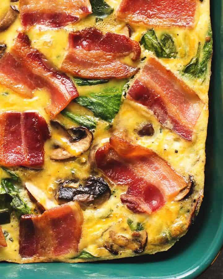 breakfast casserole with strips of bacon on top in a dark green dish