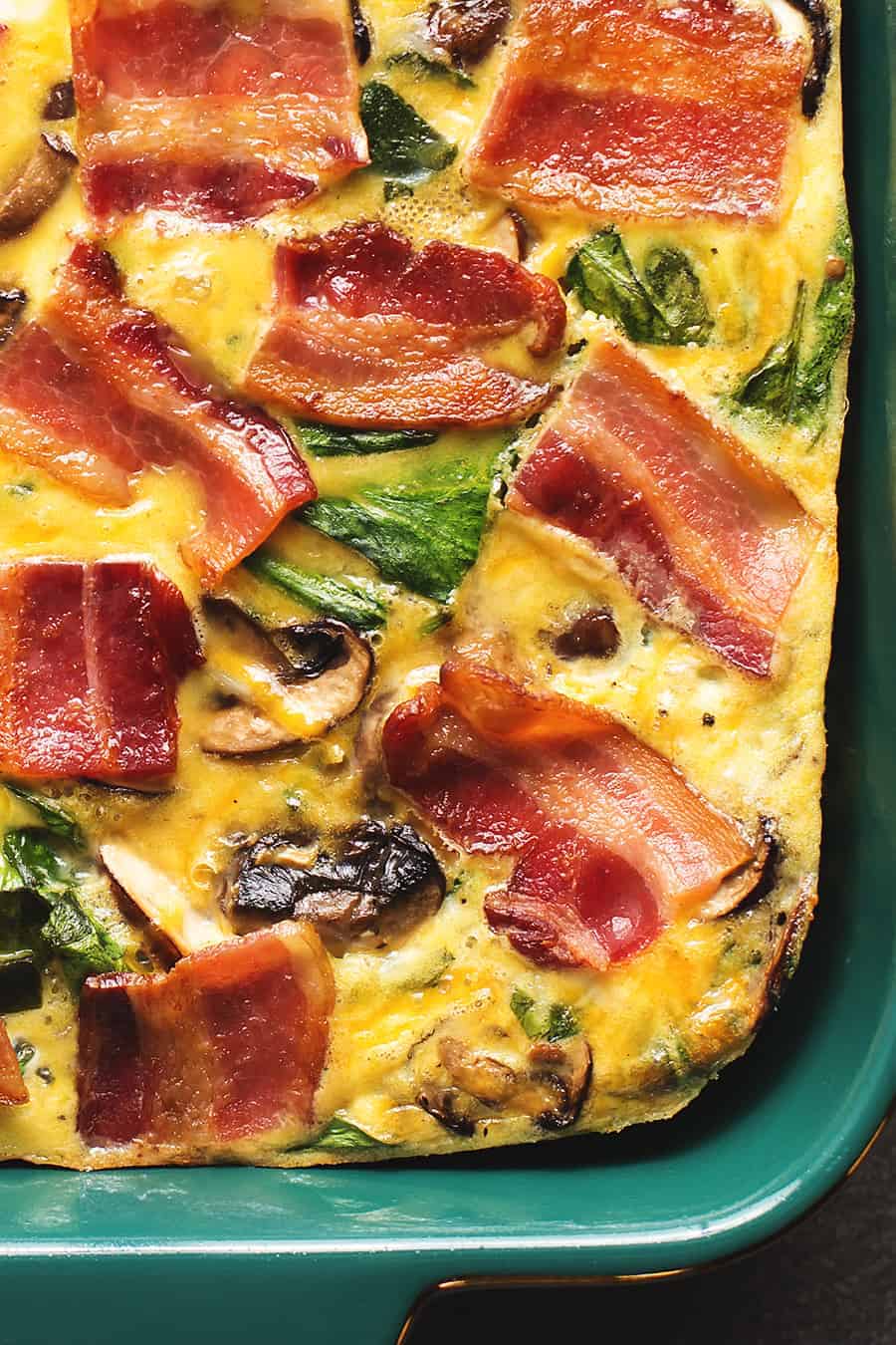 breakfast casserole with strips of bacon on top in a dark green dish