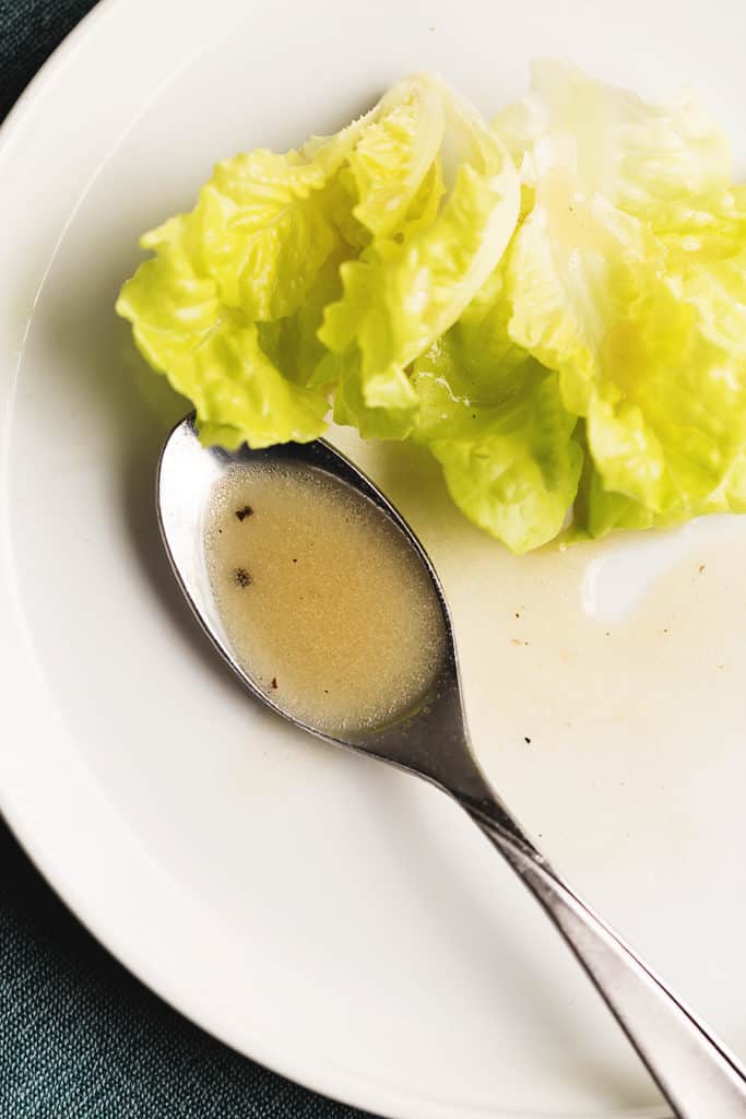 dressing on a spoon with green lettuce on a white plate