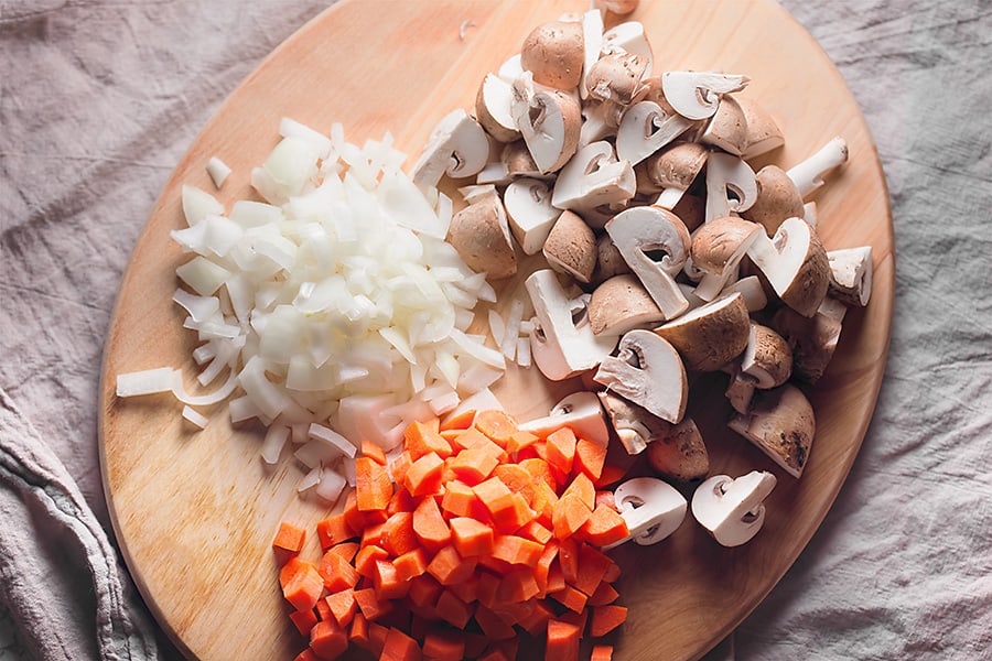 chopped mushrooms, carrots, and onions on a wood cutting board