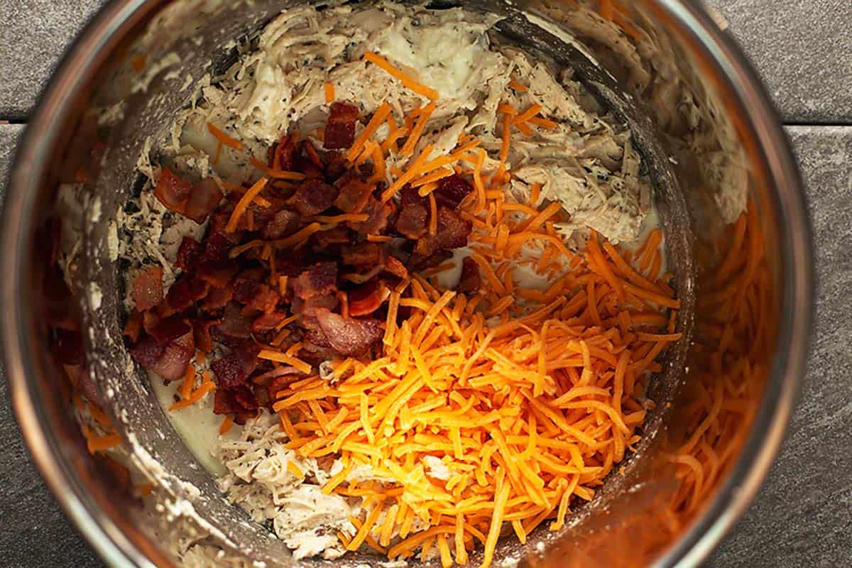 cheese and bacon on top of shredded chicken in an instant pot
