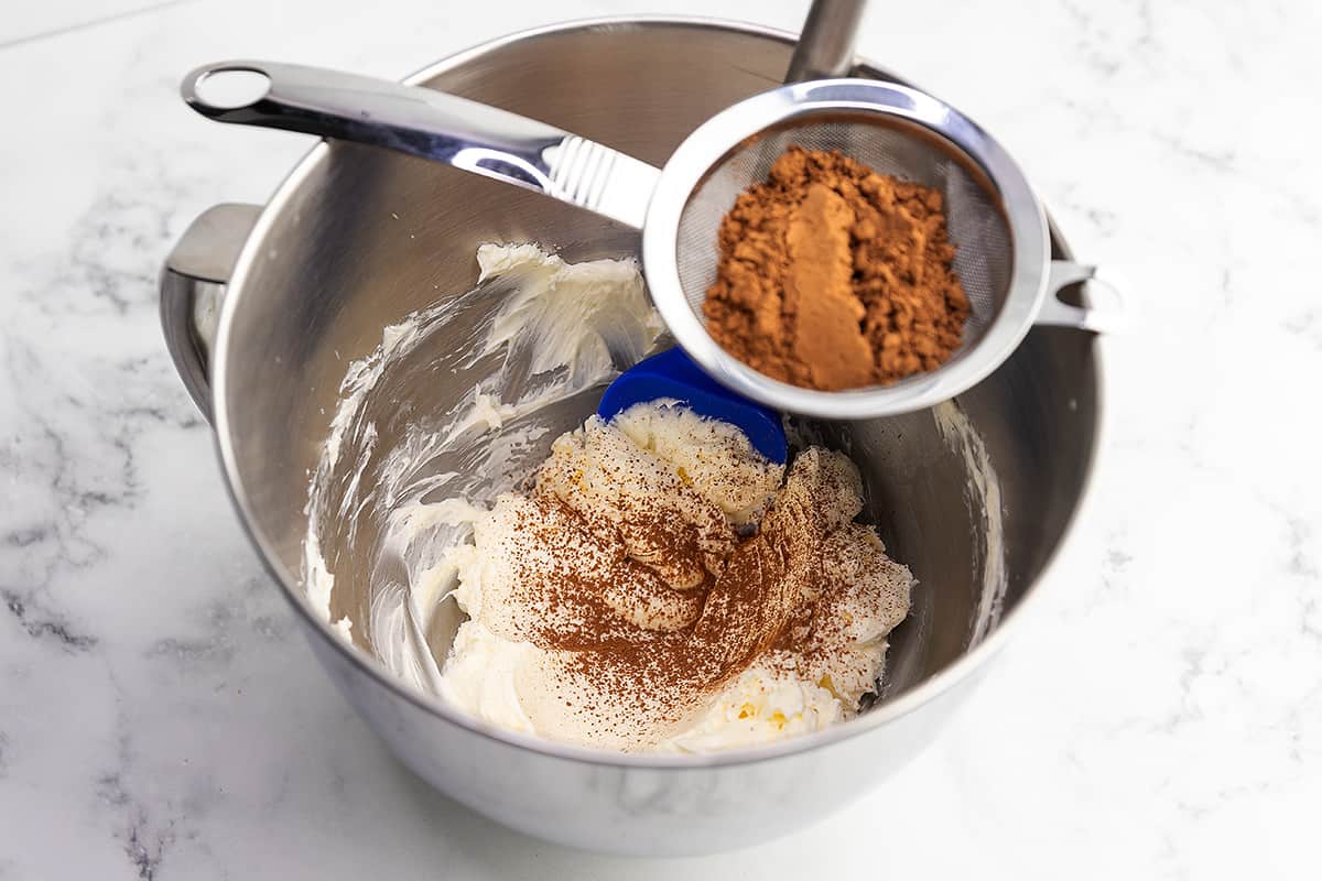 sifting cocoa powder into frosting