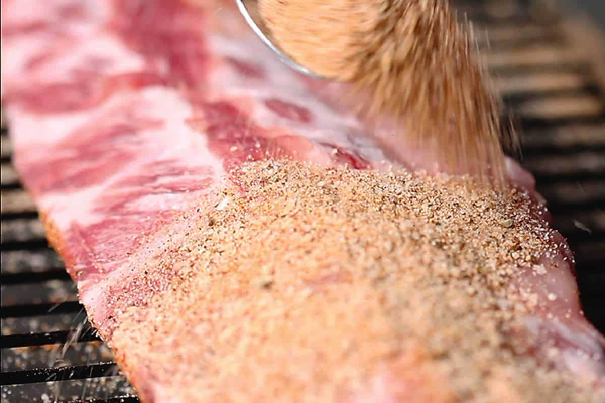 sprinkling rib rub on pork ribs