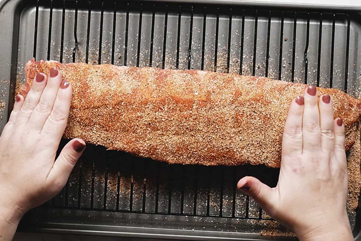 pressing bbq rib rub into a rack of ribs