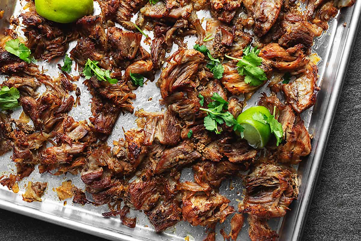 crispy carnitas on a sheet tray with limes and cilantro