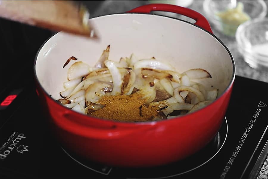 Onions frying in a red pot with curry powder