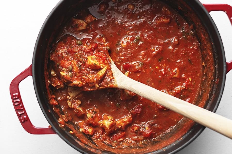 chicken cacciatore stew in a red dutch oven with a wooden spoon