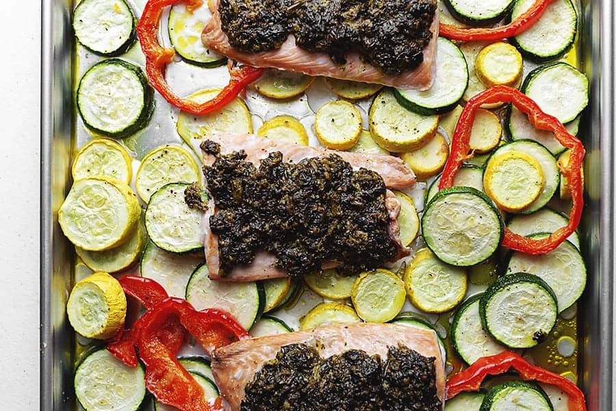 pesto topped salmon over veggies on a sheet pan