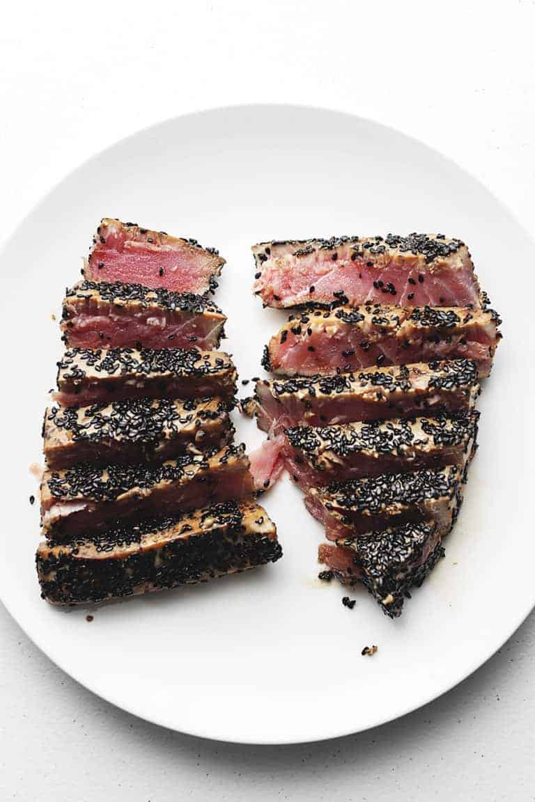 2 sesame crusted ahi tuna steaks sliced on a white plate