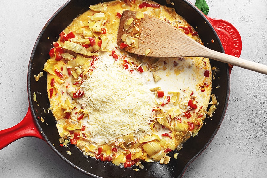 adding parmesan to vegetables in red skillet with wooden spoon