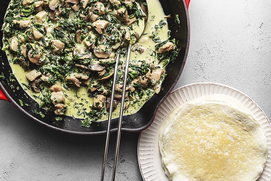 chicken Florentine being cooked in a skillet next to crepes 