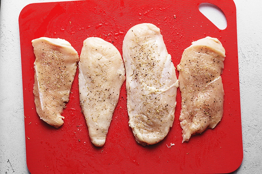 chicken breast with thyme, salt and pepper on a cutting board 