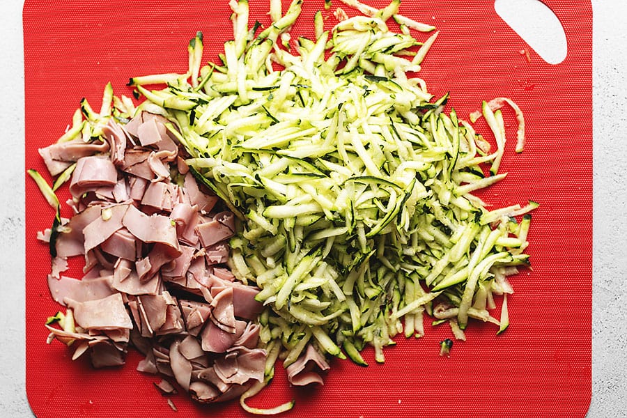 zucchini and ham being chopped up on a red cutting board