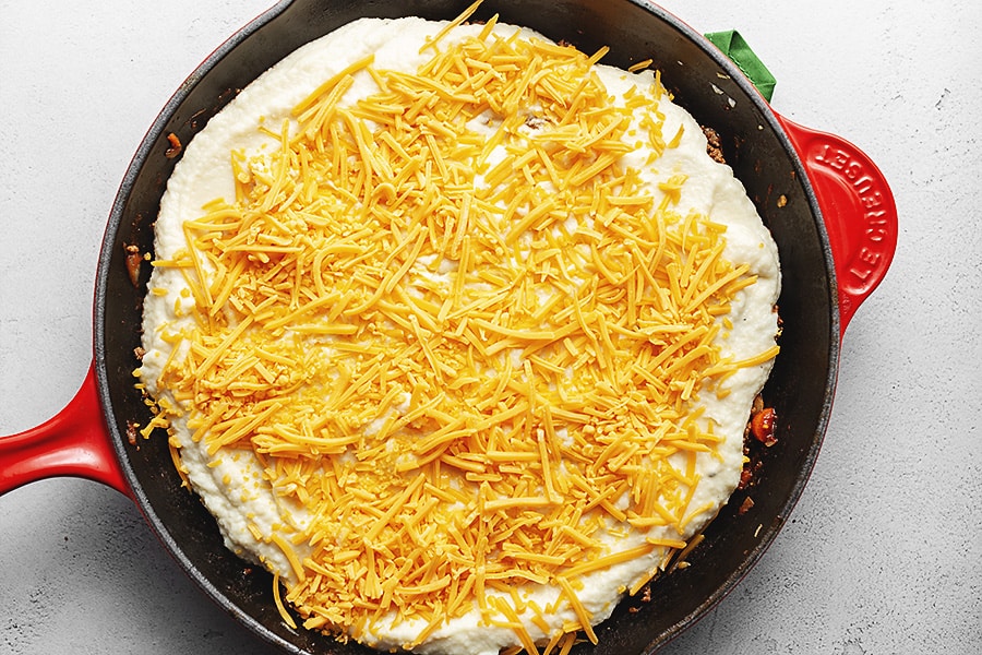 spooned mashed cauliflower with cheddar cheese on top in a skillet 