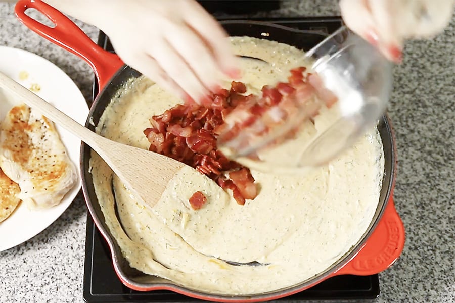 bacon being added to a cheesy sauce 