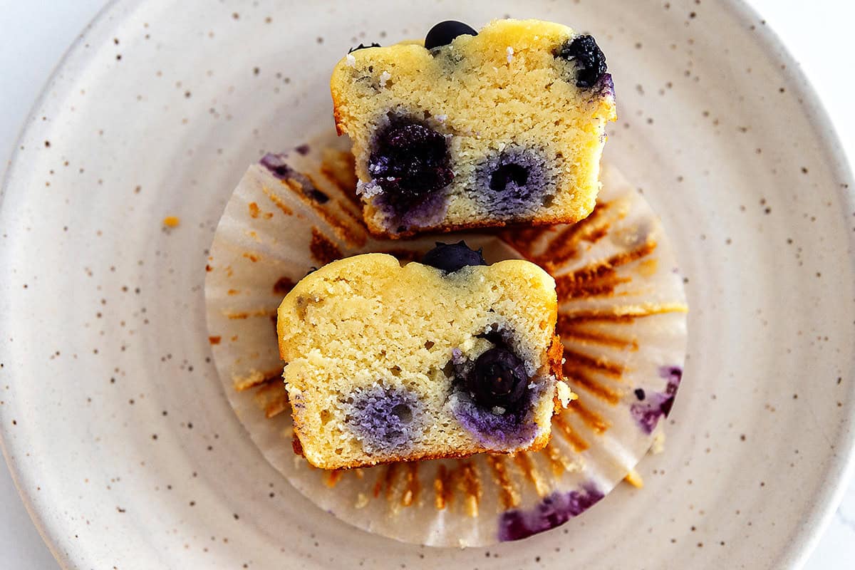 Keto blueberry muffin cut in half to show the soft, fluffy inside with blueberries throughout.