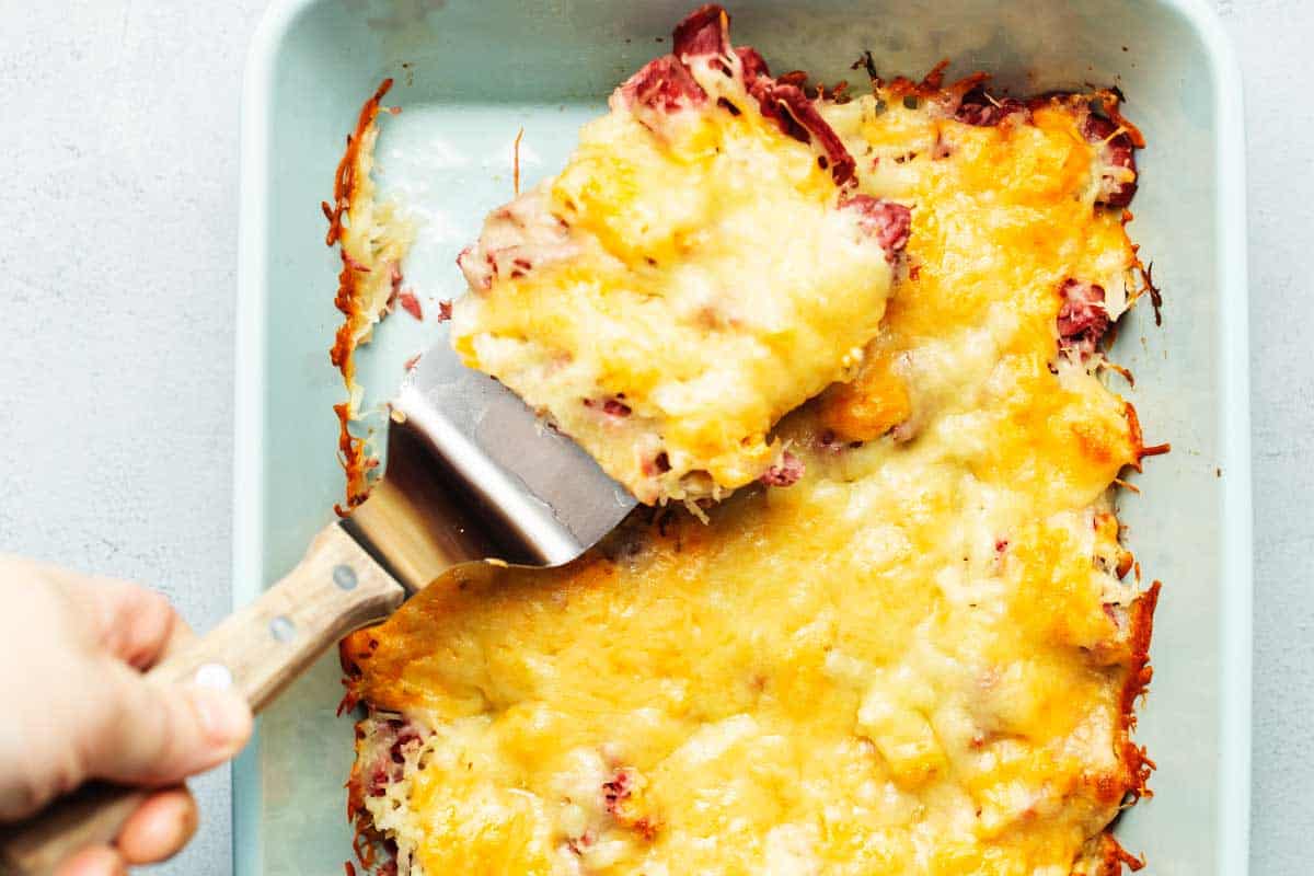 pulling a serving of keto reuben casserole out of a casserole dish