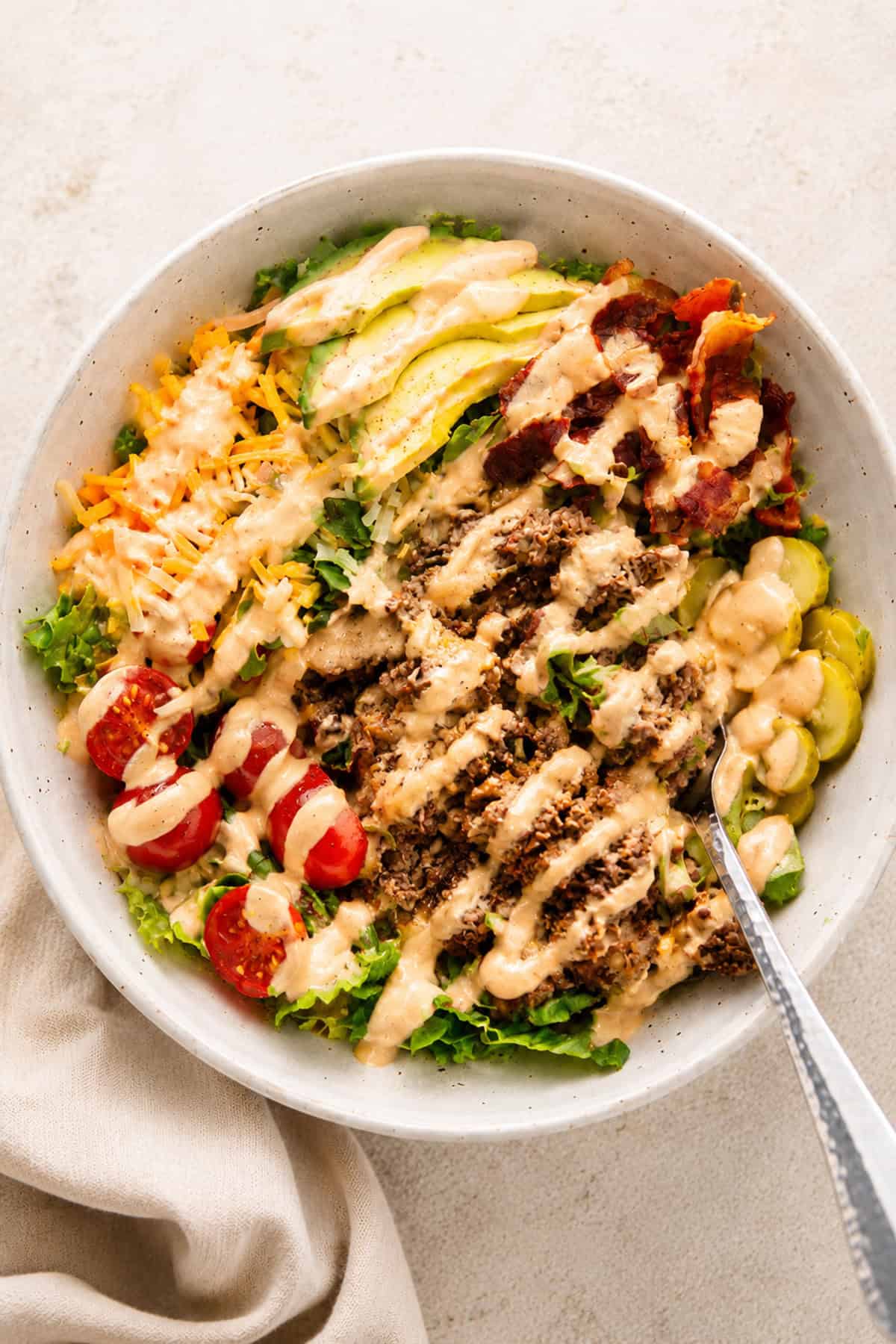 High protein Big Mac salad bowl topped with chopped burgers, crispy bacon, avocado, cheddar cheese, and burger sauce