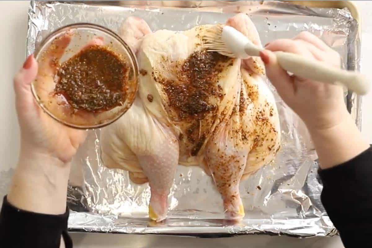 seasoning a spatchcocked chicken with a rub using a basting brush.