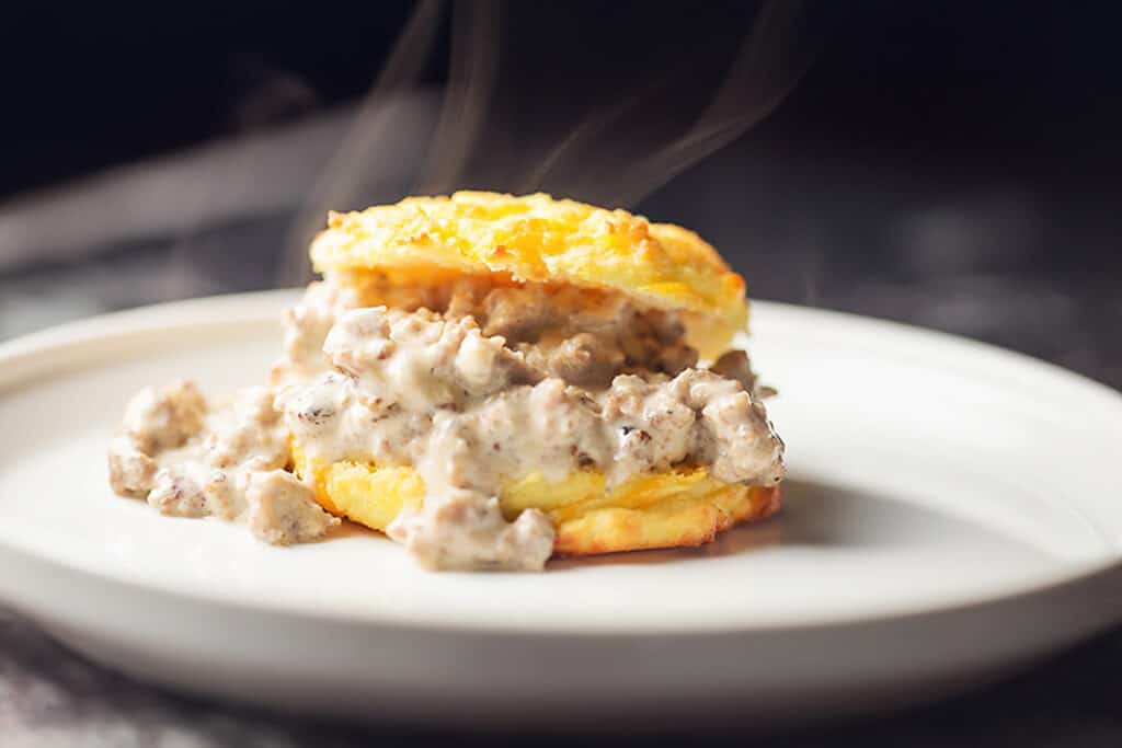 Keto biscuits and gravy on a white plate with cheddar biscuits topped with creamy sausage gravy.