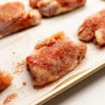 nicely seasoned boneless chicken thighs on a sheet tray lined with parchment paper.