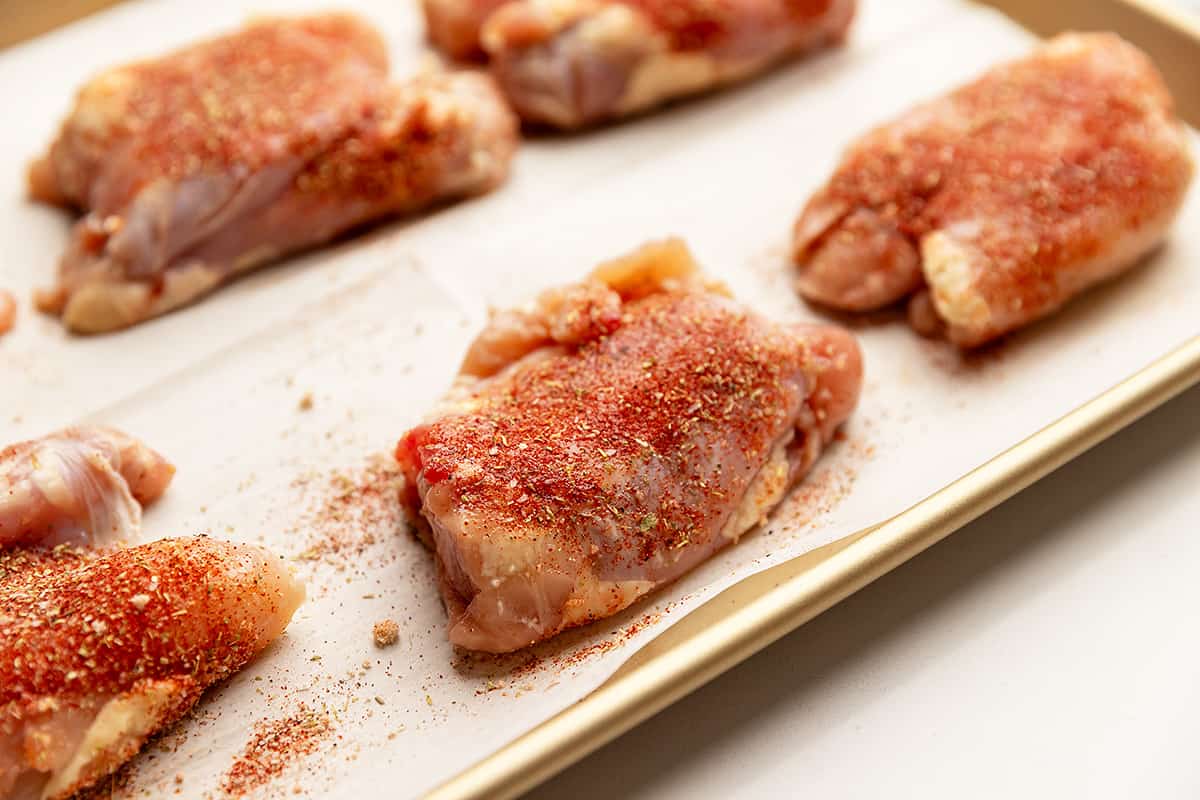 nicely seasoned boneless chicken thighs on a sheet tray lined with parchment paper.