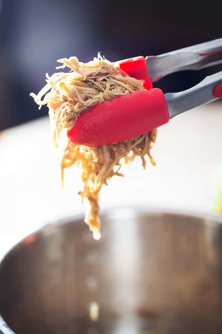 using tongs to pull shredded chicken out of an instant pot