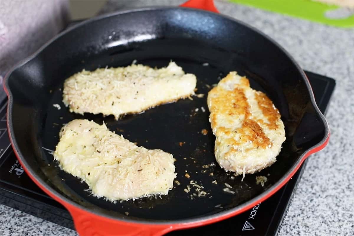 cooking parmesan coated chicken breast in a skillet