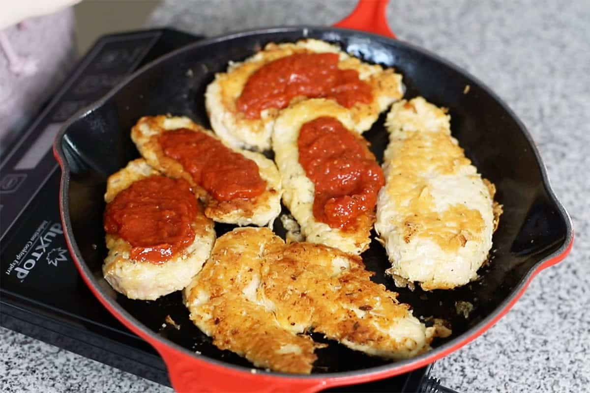 spooning marinara sauce on chicken breast