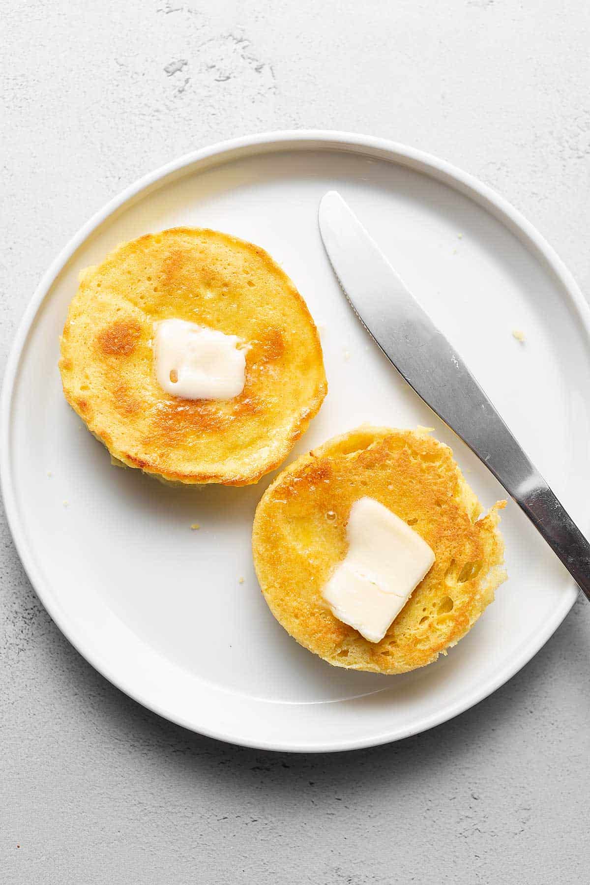 keto English muffins on a white plate with butter and a knife