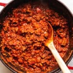 Using a wooden spoon to scoop chili out of a red pot