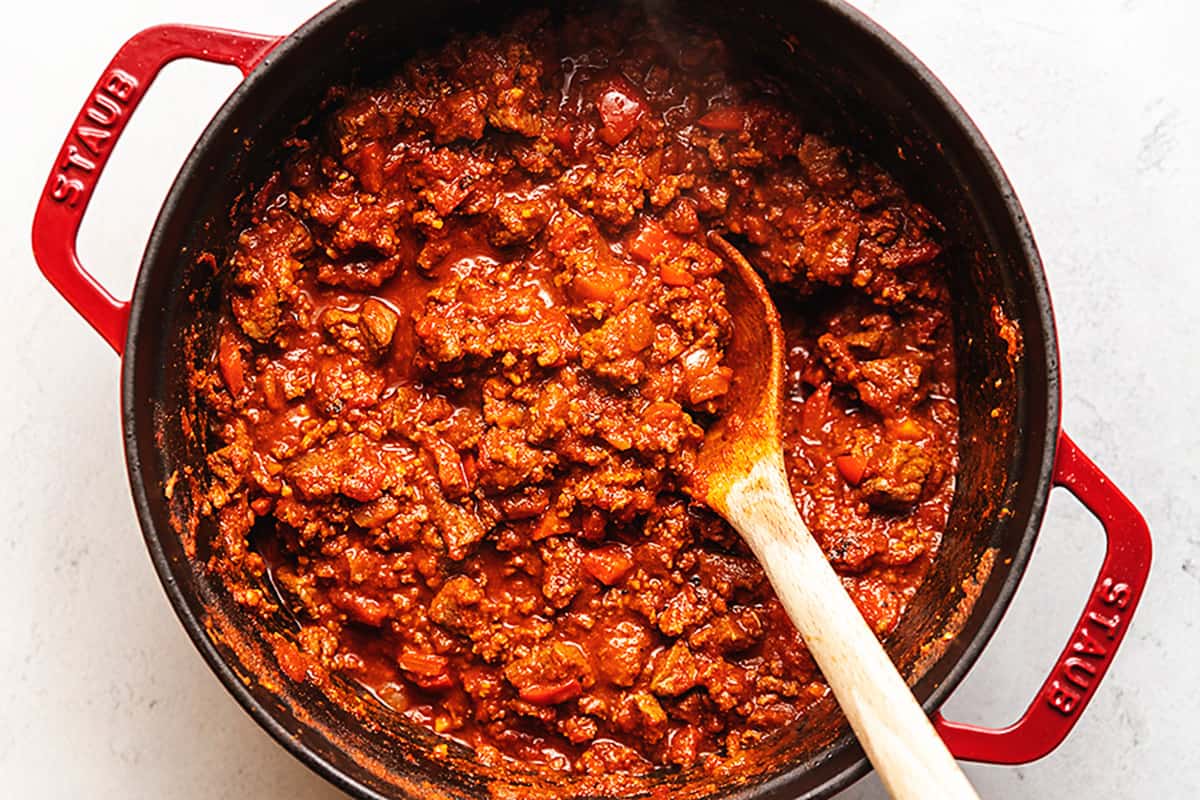 Using a wooden spoon to scoop chili out of a red pot