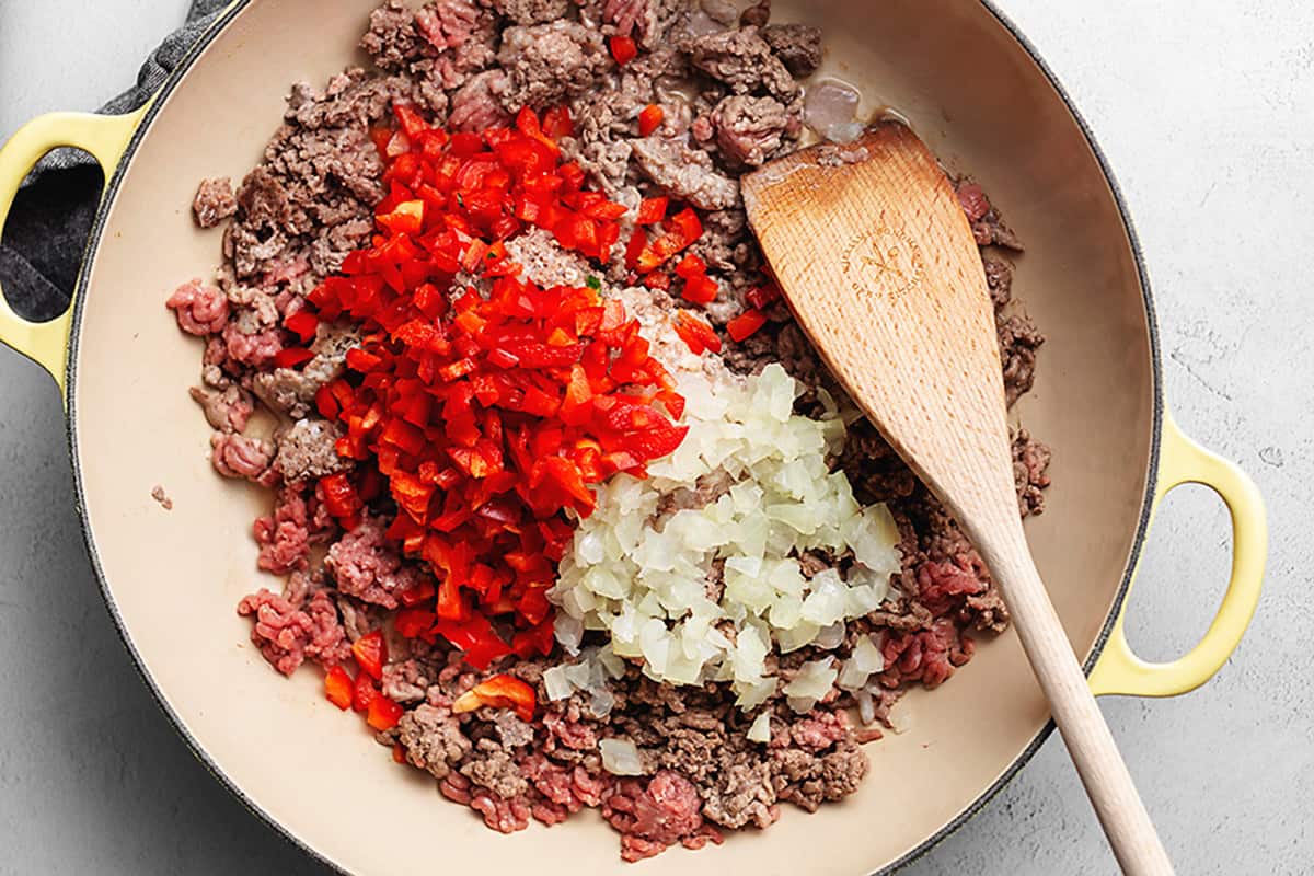 adding bell pepper and onion to sloppy Joe meat in a skillet