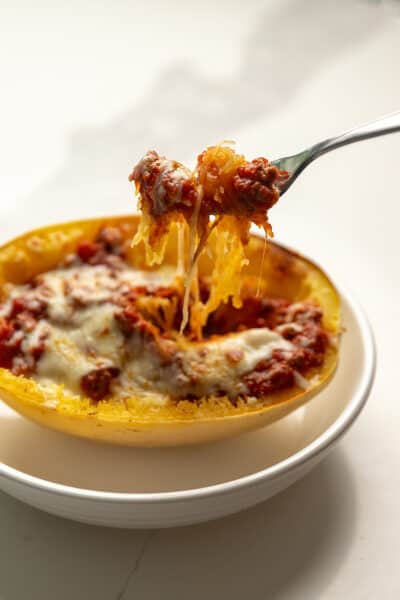 a fork pulling squash noodles out of a stuffed spaghetti squash boat