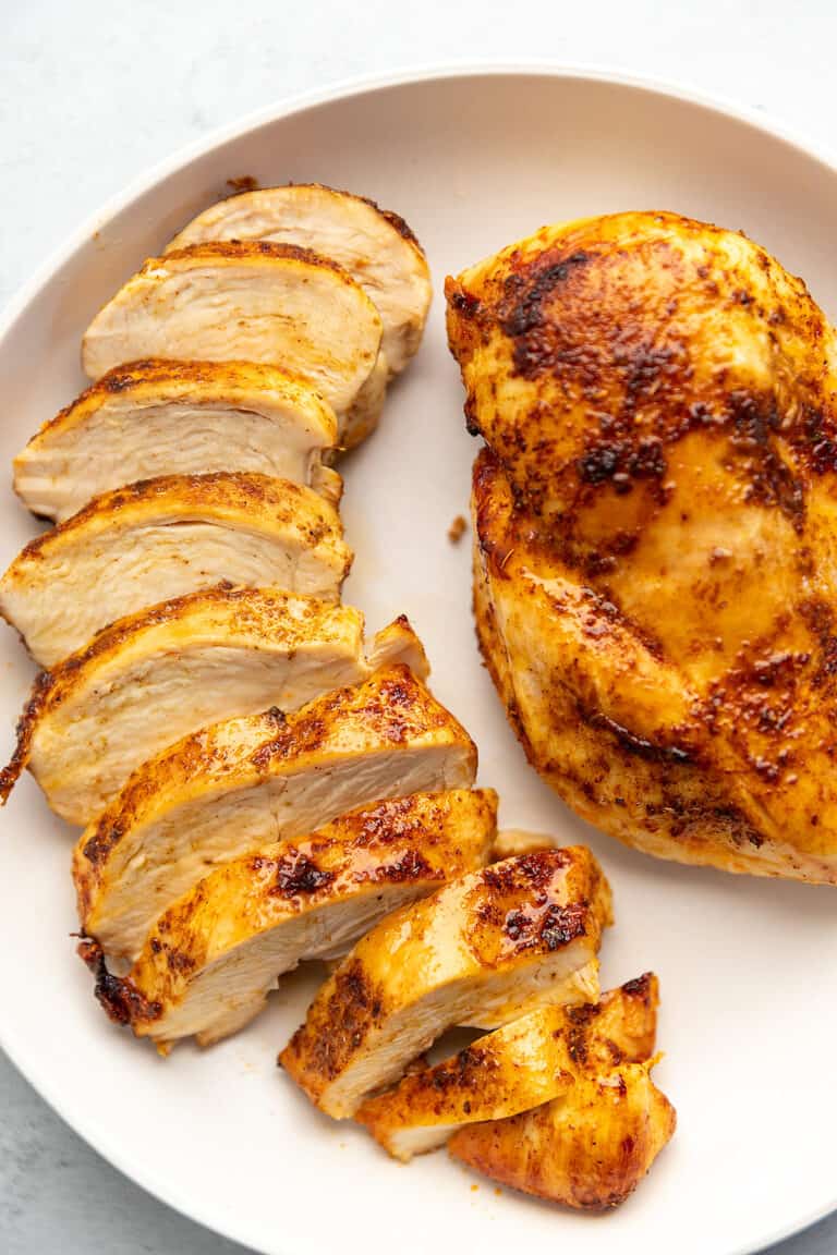 a white plate with one perfect chicken breast uncut, and one cut into strips.