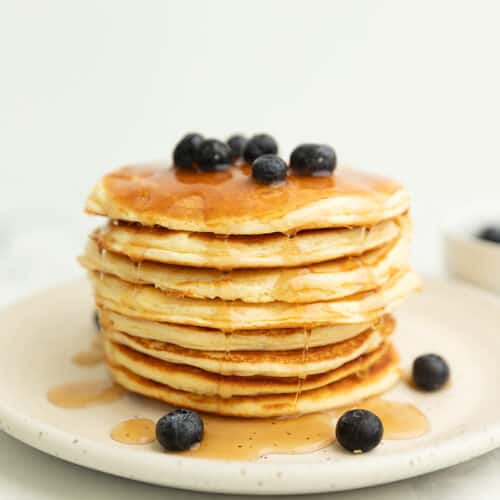 a big stack of pancakes on a white plate with blueberries