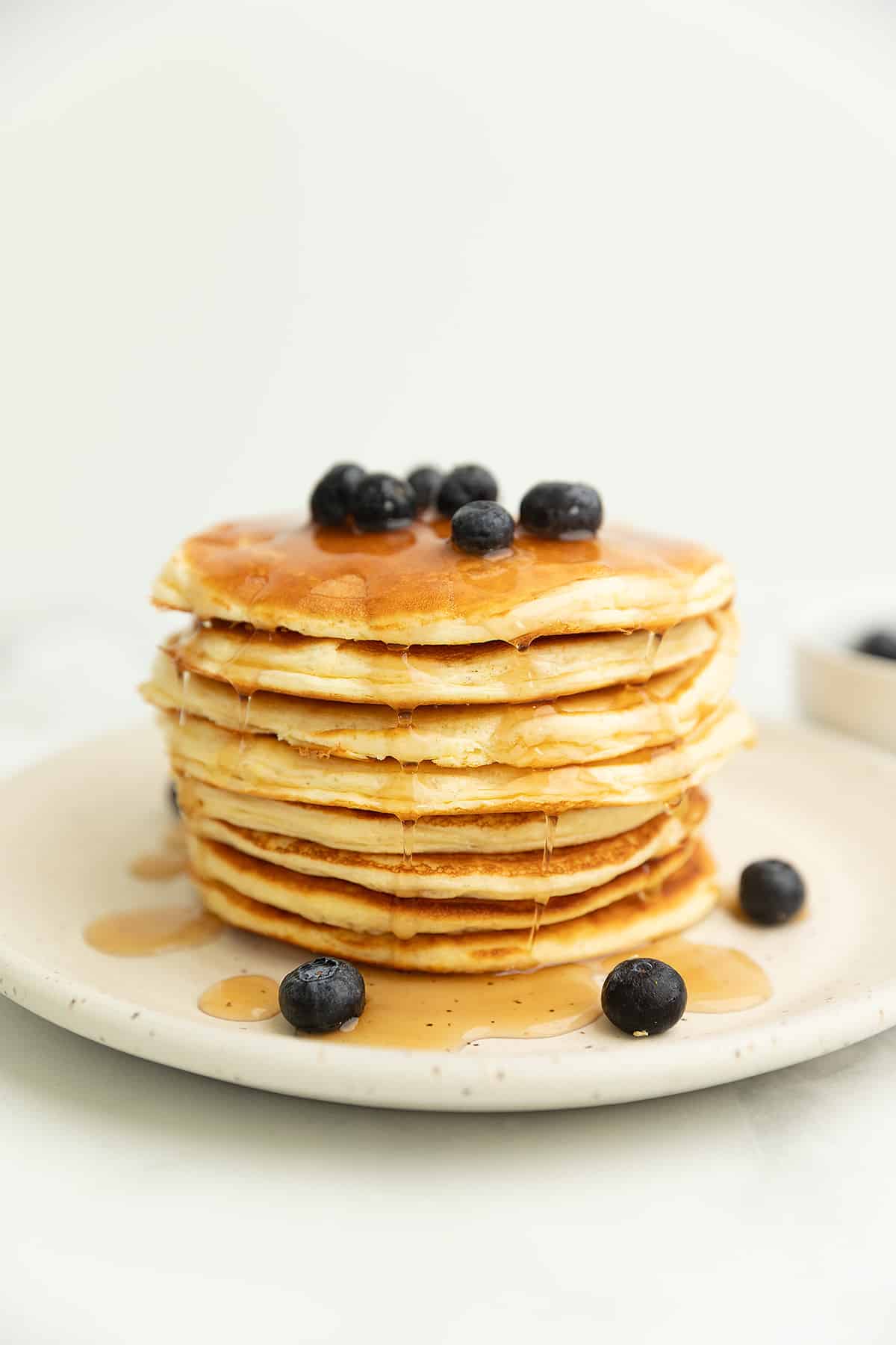 a stack of protein pancakes on a white plate with blueberries and syrup