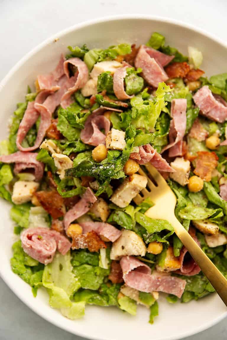 a salad with salami in a white bowl