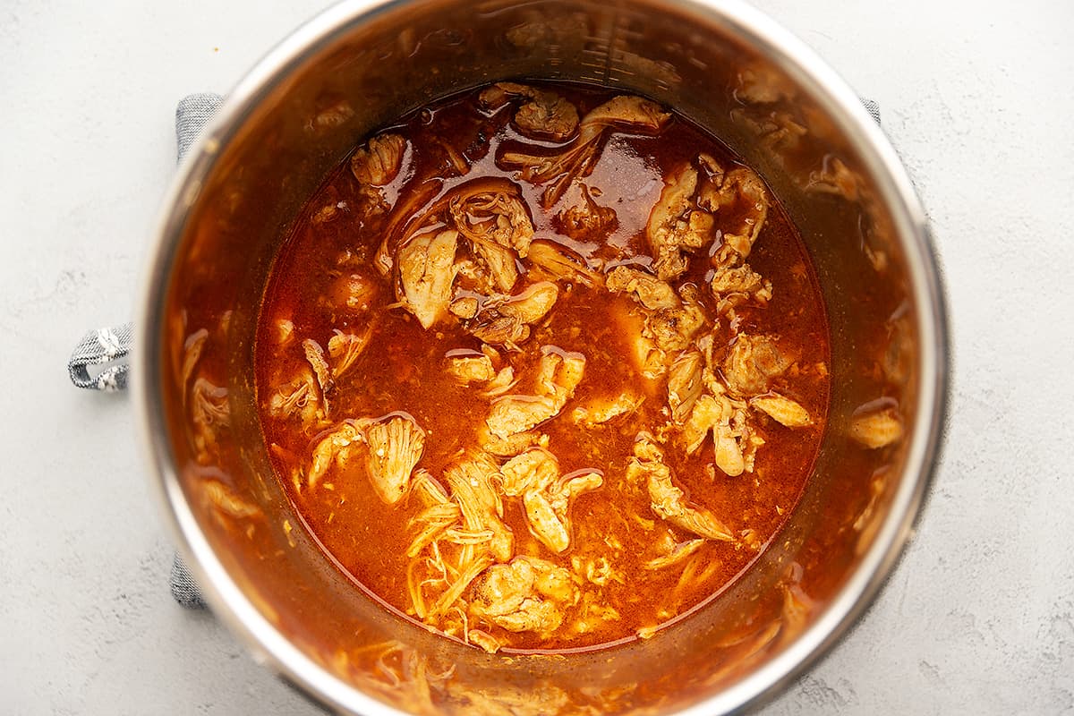 a pot with shredded chicken in a red sauce
