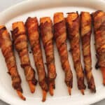 cooked bacon wrapped carrots on a white platter
